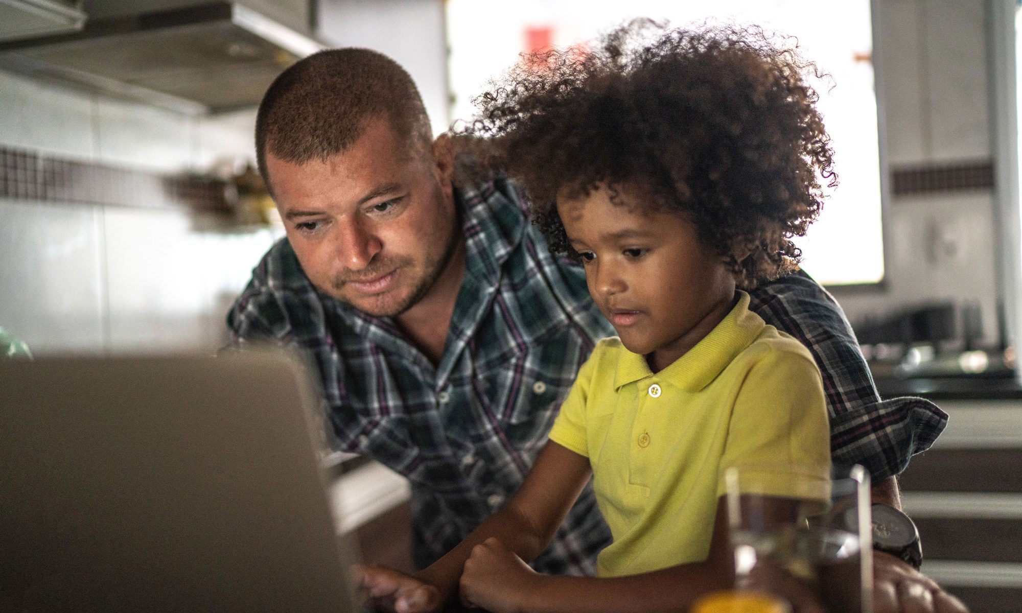 Father helps child with homework on laptop
