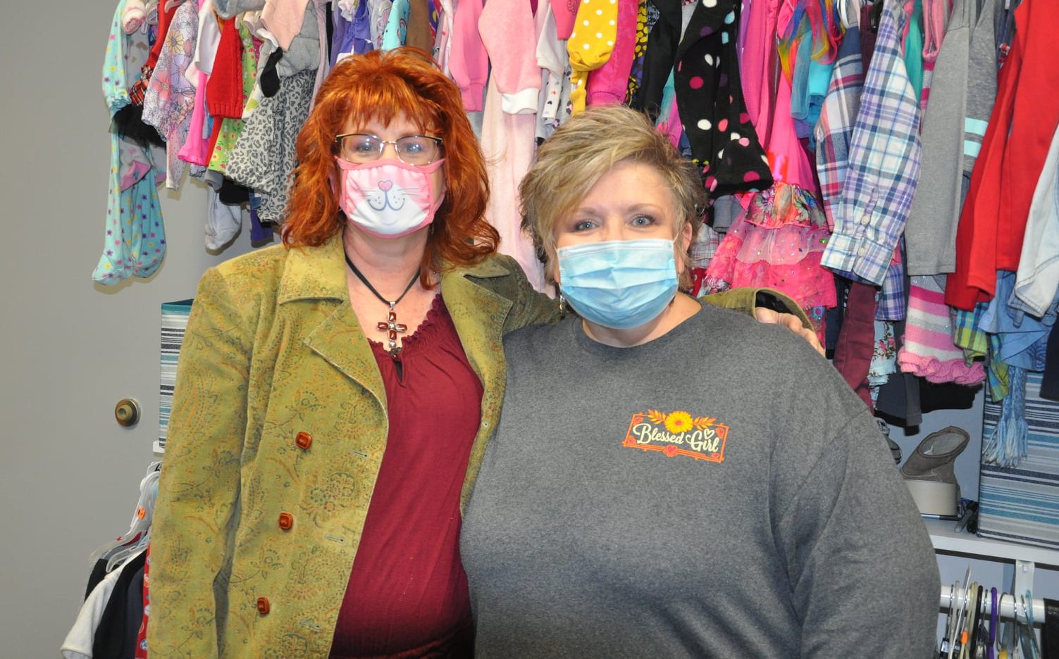 Two women wearing medical masks standing in front of racks of clothing