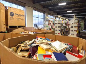 Warehouse with books inside of a large cardboard container and also on industrial shelving